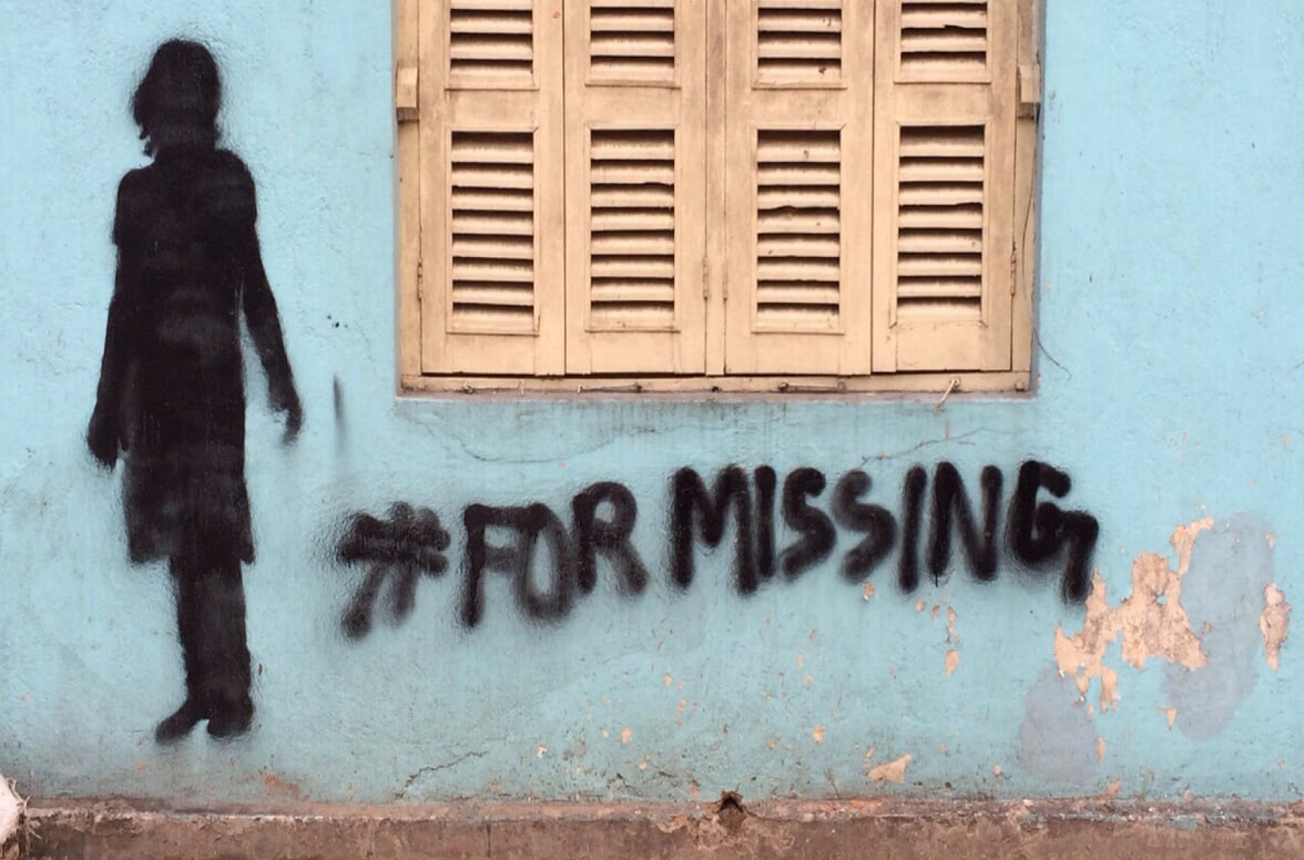Silhouette of a girl and the hashtag #FORMISSING, painted on an old wall beside a shuttered window
