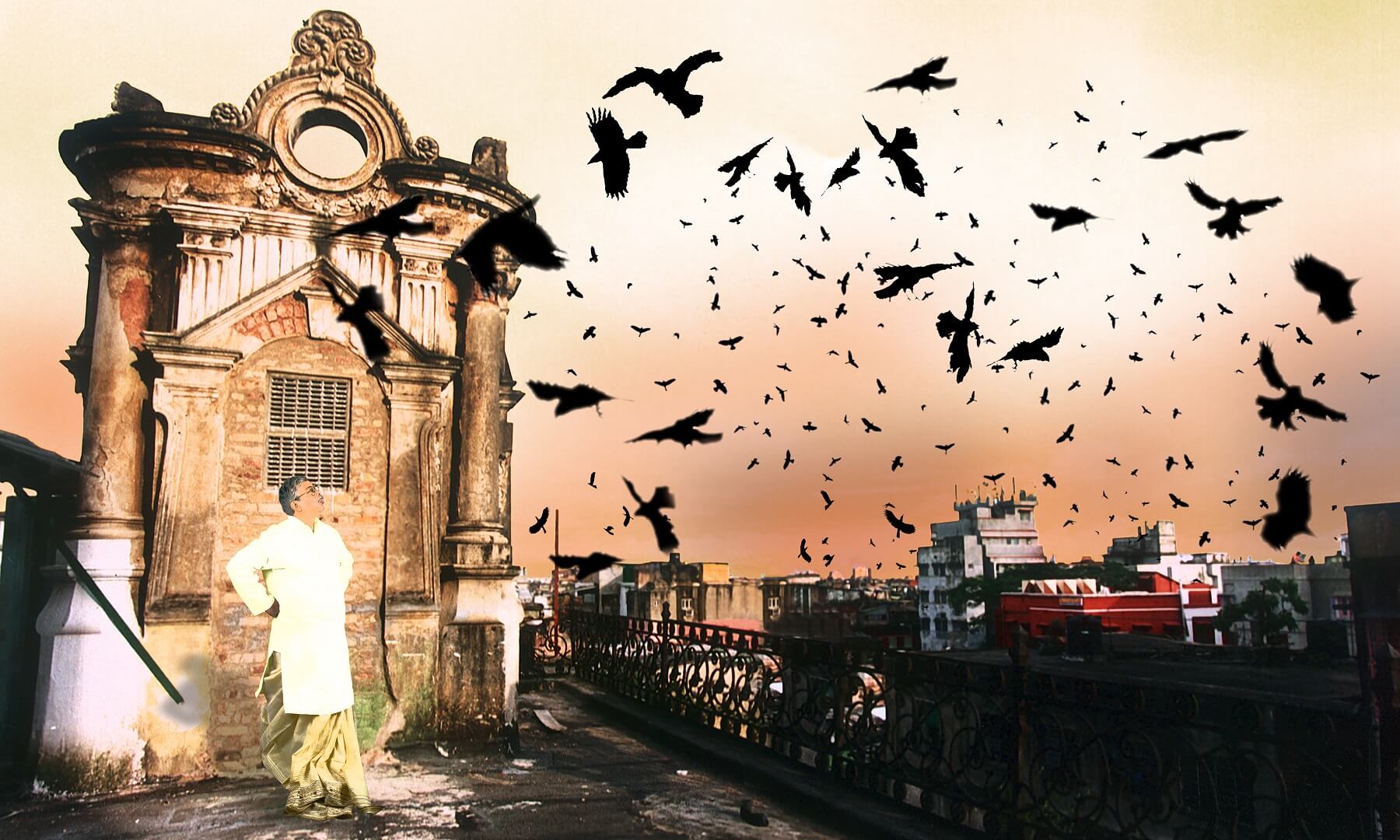 A Bengali Babu in traditional attire stands on a terrace near an old building, watching birds fly across the sky
