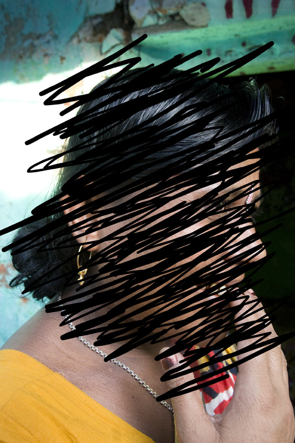 A woman in yellow with gold earrings and a silver chain touches her face, partly obscured by expressive black markings