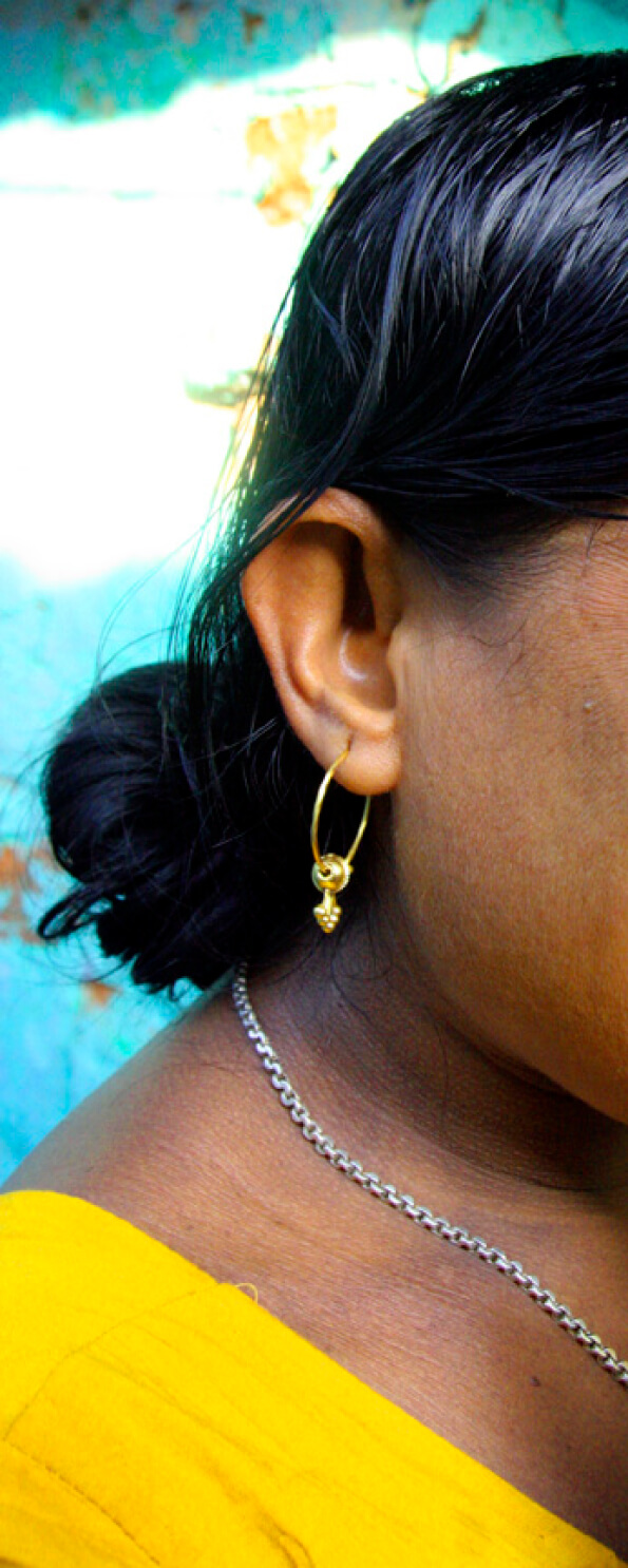 A close-up of a woman's ear adorned with a gold earring, with her hair tied back and a silver chain necklace visible