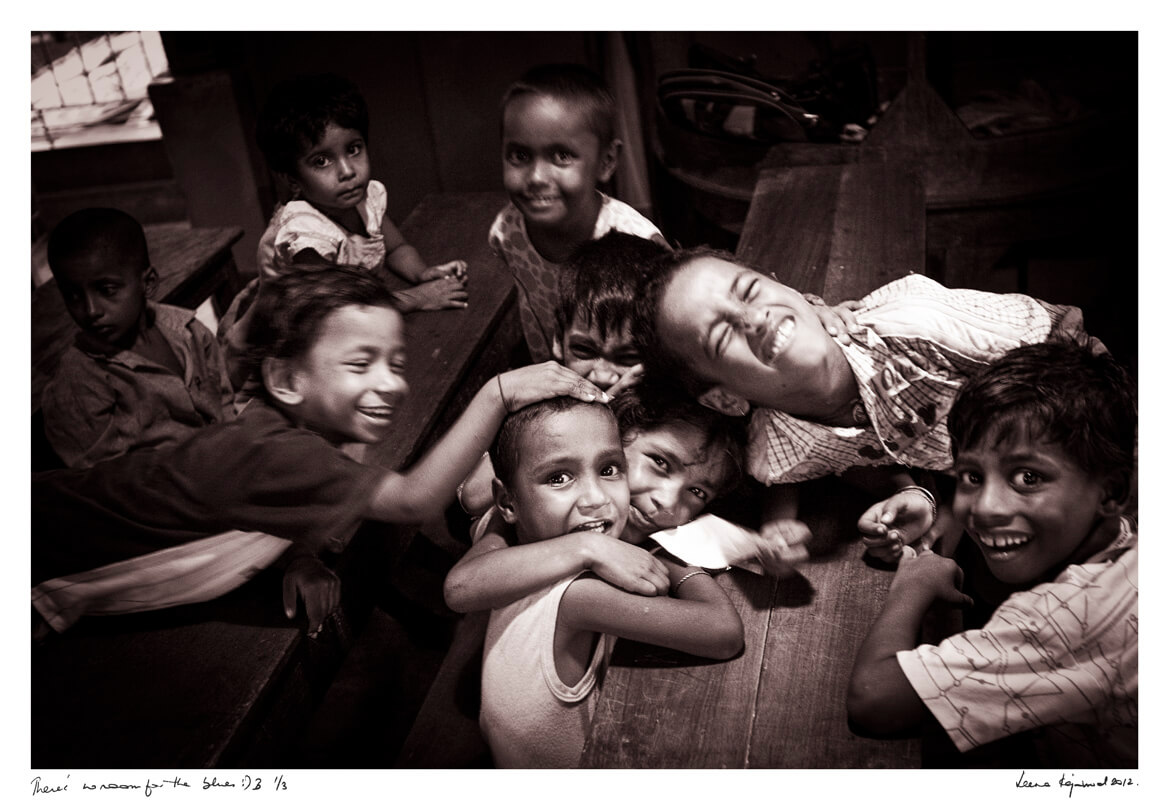 A group of children sit closely on wooden benches, some smiling while others lean on each other or look toward the camera