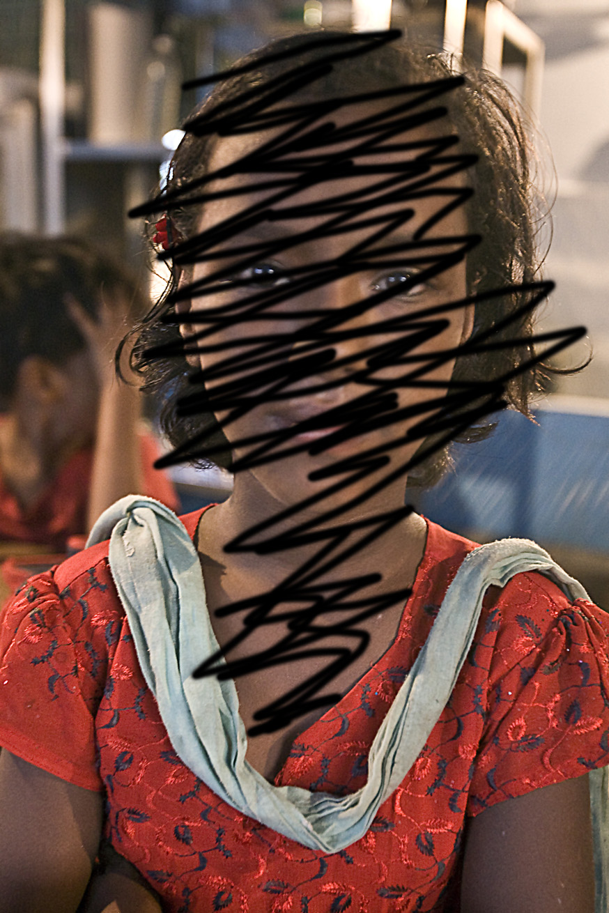 A person in red with a blue scarf stands indoors, face obscured, with another figure slightly blurred in the background