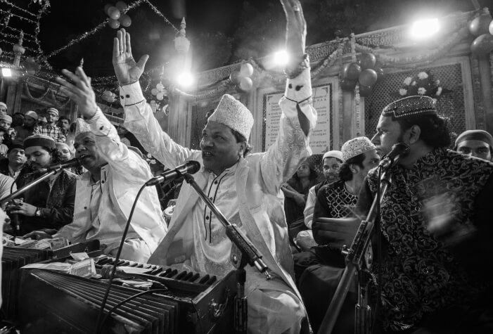 A qawwali singer performs with expressive gestures alongside fellow musicians at a nighttime gathering