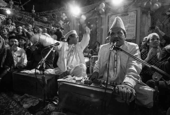 Qawwali singers, with musicians on harmoniums and microphones, perform passionately, captivating the audience with their energy