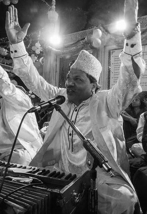A qawwali singer performs with expressive gestures alongside fellow musicians at a nighttime gathering