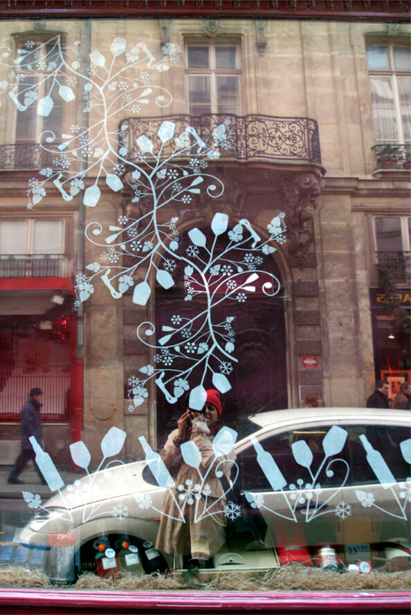 A window with white floral patterns reflects a person taking a photo, parked cars, and historic buildings