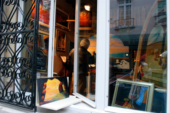 A view through an open window of an art gallery, showing colorful paintings and a person admiring the displayed artwork