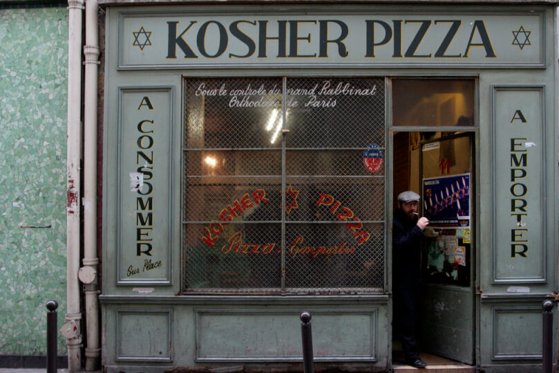 A storefront labeled "Kosher Pizza" with a green facade shows a man in a cap stepping out of the partially open door
