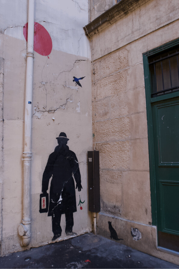 A stencil-style street art on a wall shows a shadowy figure with a briefcase, accompanied by a cat, bird, and balloon